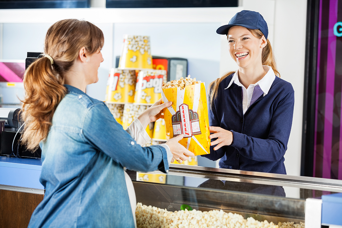 Female concession worker handing popcorn to customer