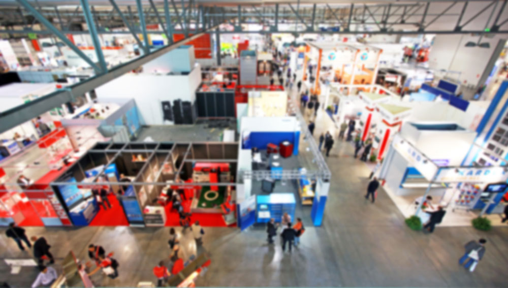 Blurred trade show floor with blue and red booths