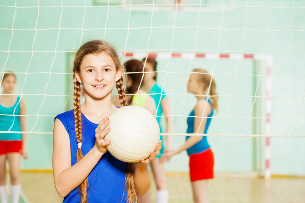 Girl holding volleyball in front of net