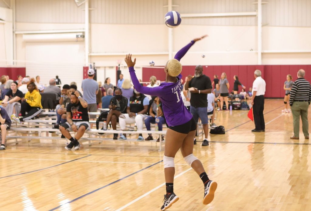 A player in a purple jersey serves the ball overhead at a volleyball tournament at Rocky Mount Event Center.